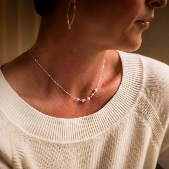 Woman's neckline wearing a white sweater with 16 inch gold freshwater pearl layering necklace with 5 pearls and gold threader earrings. Eden Necklace by Sarah Cornwell Jewelry
