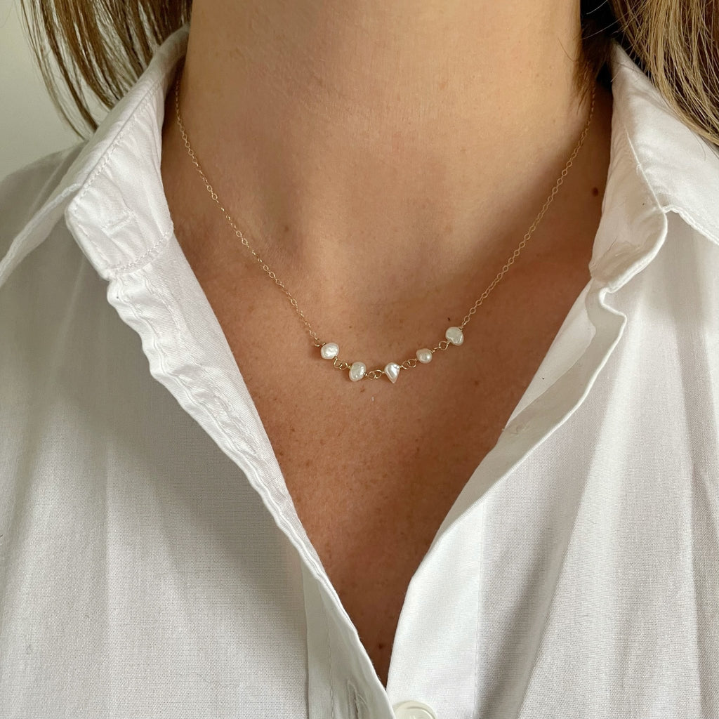 Woman's neckline wearing a white button down shirt with 16 inch gold freshwater pearl layering necklace with 5 pearls. Eden Necklace by Sarah Cornwell Jewelry