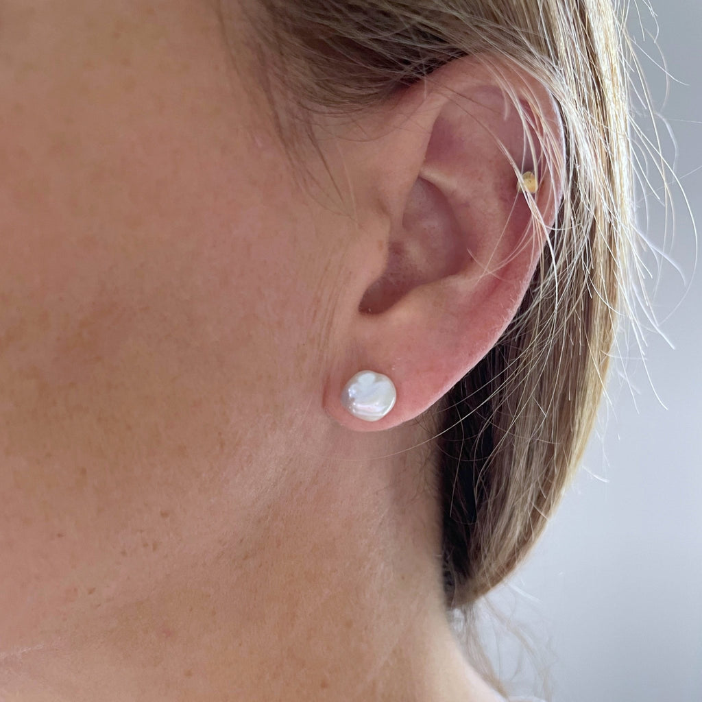 Woman with blonde hair wearing pearl stud earrings with 8-9 mm white freshwater keshi pearl and a gold stud earring. Etta Studs by Sarah Cornwell Jewelry