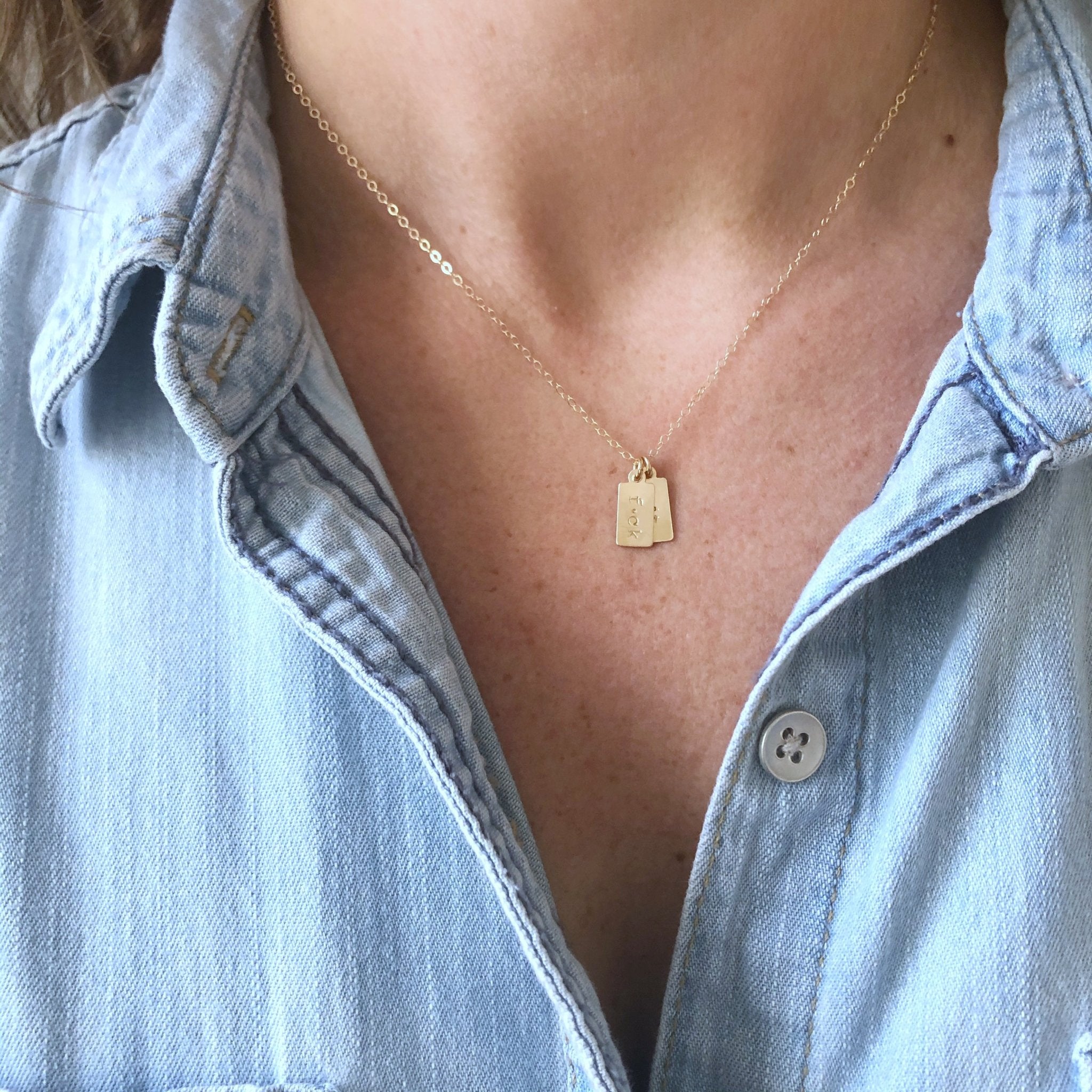 Woman's neckline wearing a denim button down with gold double tag "fuck it" layering necklace. F*ck It Necklace by Sarah Cornwell Jewelry