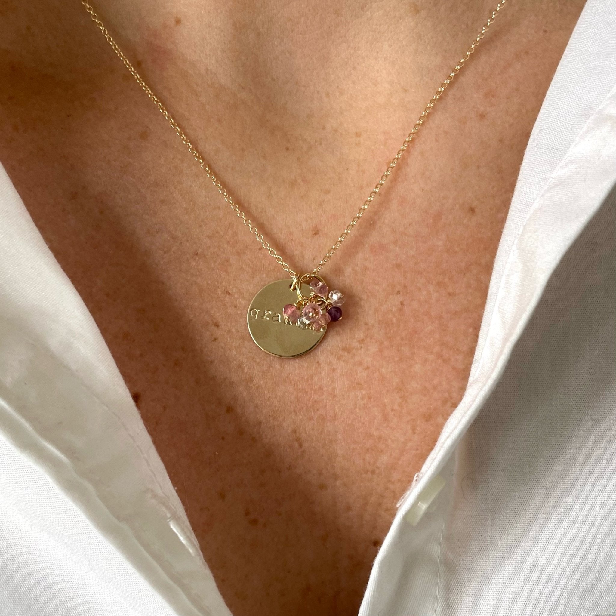 Woman's neckline wearing white button down with gold grandma disc and wire wrapped gemstone necklace with 7 pink, white, light blue and purple gemstones. Gigi Necklace by Sarah Cornwell Jewelry