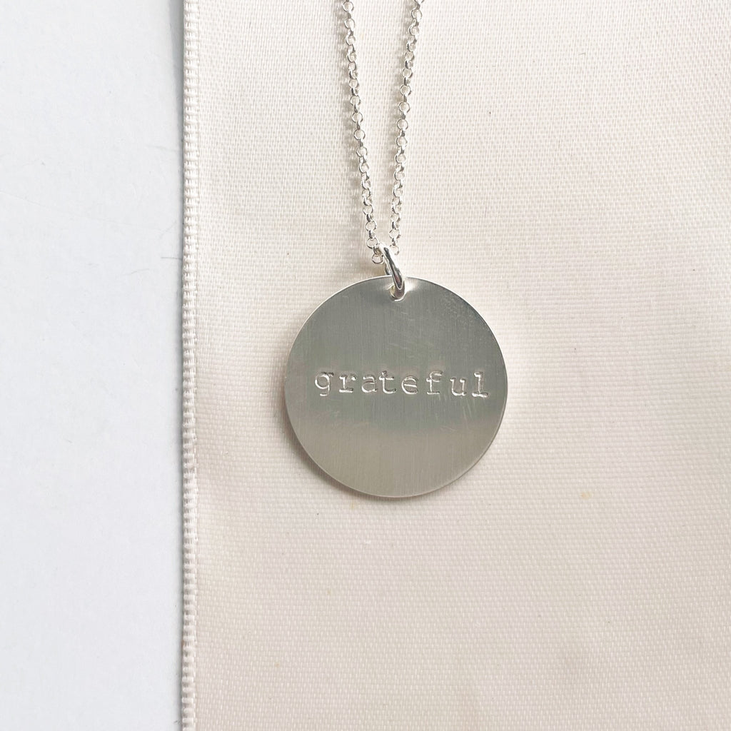 28 inch silver necklace with 3/4 inch stamped disc with the word grateful. Hana Necklace by Sarah Cornwell Jewelry