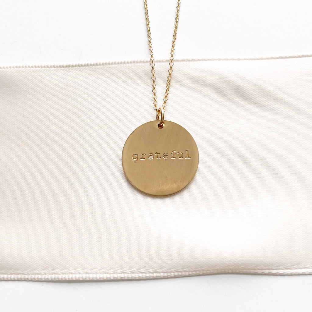 28 inch gold necklace with 3/4 inch stamped disc with the word grateful. Hana Necklace by Sarah Cornwell Jewelry