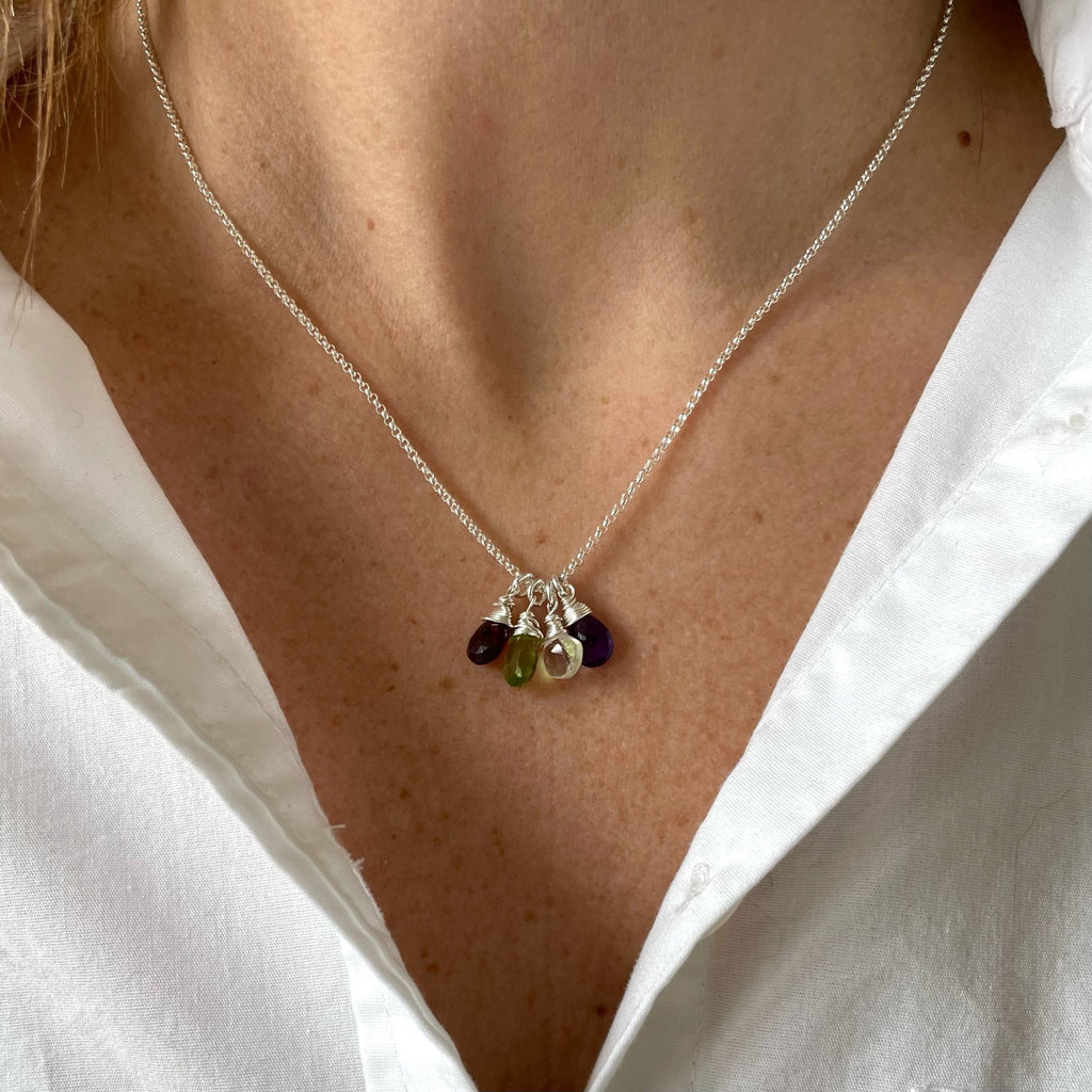 Woman's neckline wearing white button down shirt with silver wire wrapped gemstone birthstone necklace with red, light green, light yellow and purple gemstone pendants. Heritage Necklace by Sarah Cornwell Jewelry