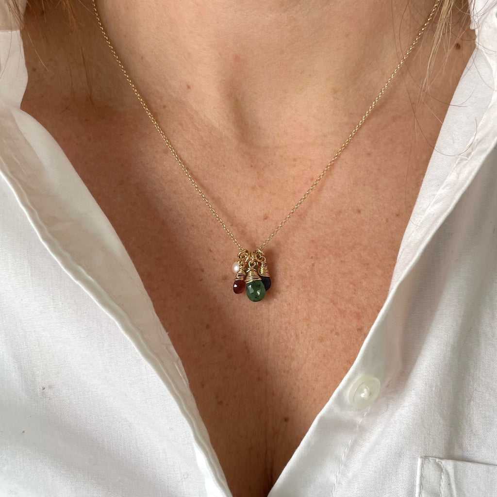Woman's neckline wearing white button down shirt with gold wire wrapped gemstone birthstone necklace with pearl and blue, green and red gemstone pendants. Heritage Necklace by Sarah Cornwell Jewelry