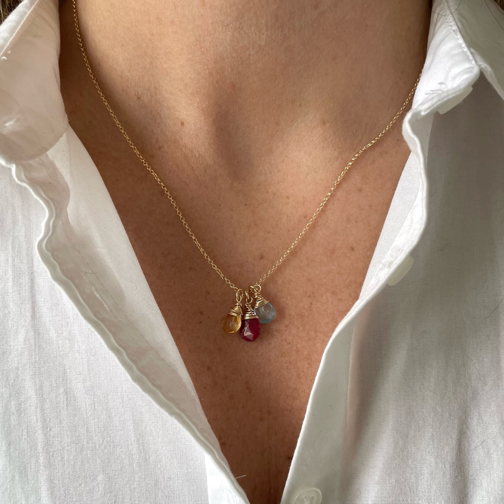 Woman's neckline wearing white button down shirt with gold wire wrapped gemstone birthstone necklace with yellow, red and light blue gemstone pendants. Heritage Necklace by Sarah Cornwell Jewelry
