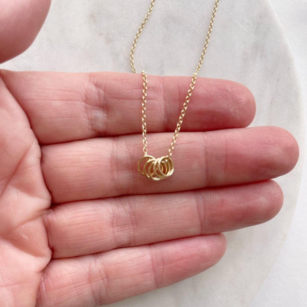Hand holding gold necklace with 5 tiny gold rings. Honor Necklace by Sarah Cornwell Jewelry