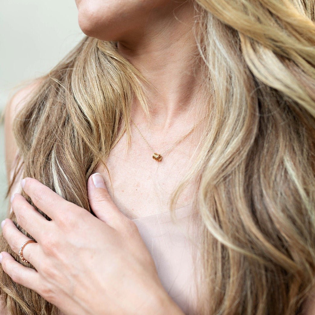 Woman's neckline with blonde hair wearing beige tank top with gold necklace with 5 tiny gold rings and pearl and textured disc drop earrings. Honor Necklace by Sarah Cornwell Jewelry