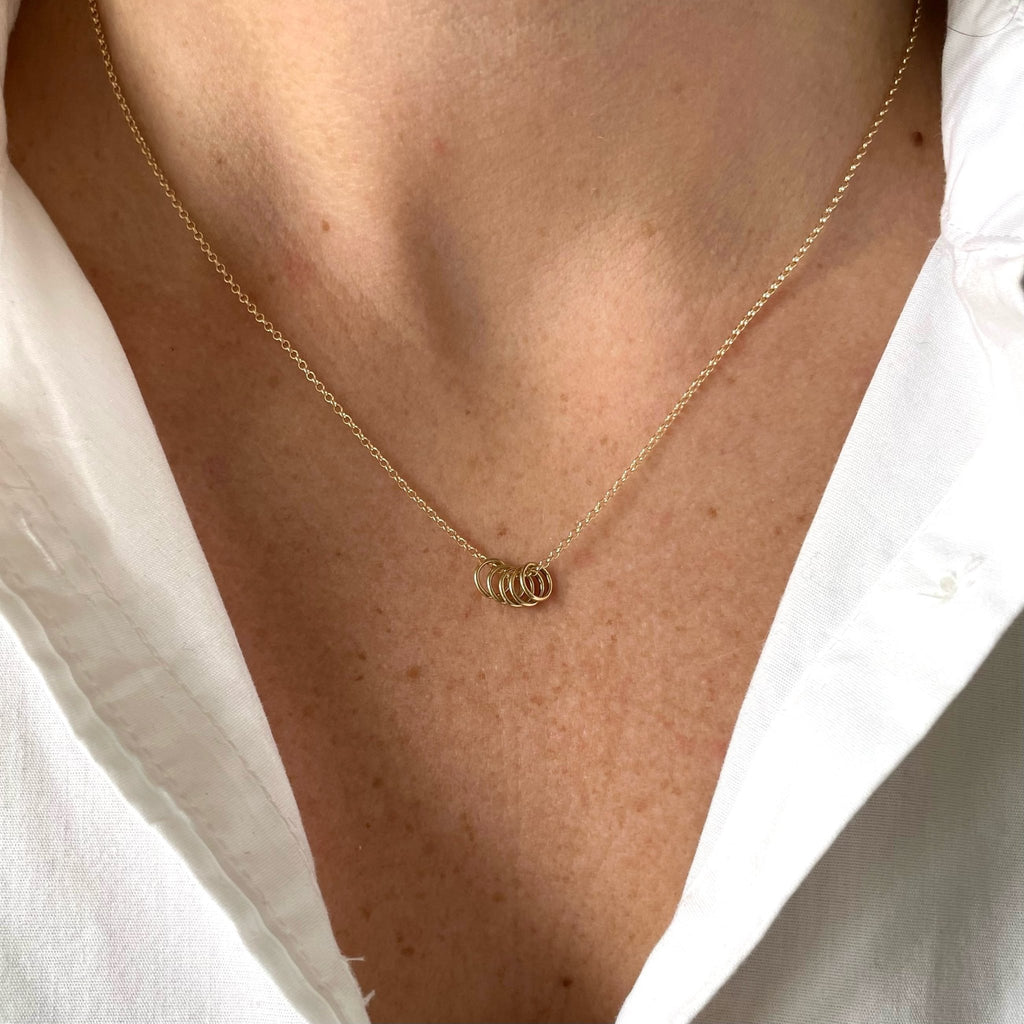 Woman's neckline wearing white button down with gold necklace with 5 tiny gold rings. Honor Necklace by Sarah Cornwell Jewelry