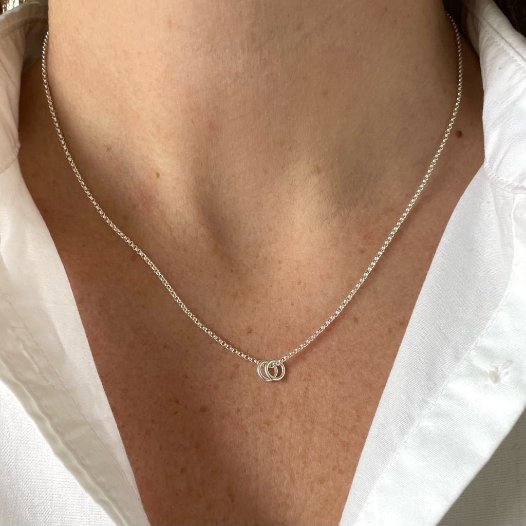 Woman's neckline wearing white button down with silver necklace with 2 tiny gold rings. Honor Necklace by Sarah Cornwell Jewelry