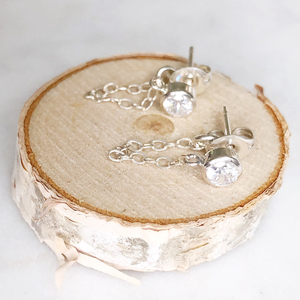 3mm white topaz and gold chain stud earrings displayed on a wood round. Kate Studs by Sarah Cornwell Jewelry