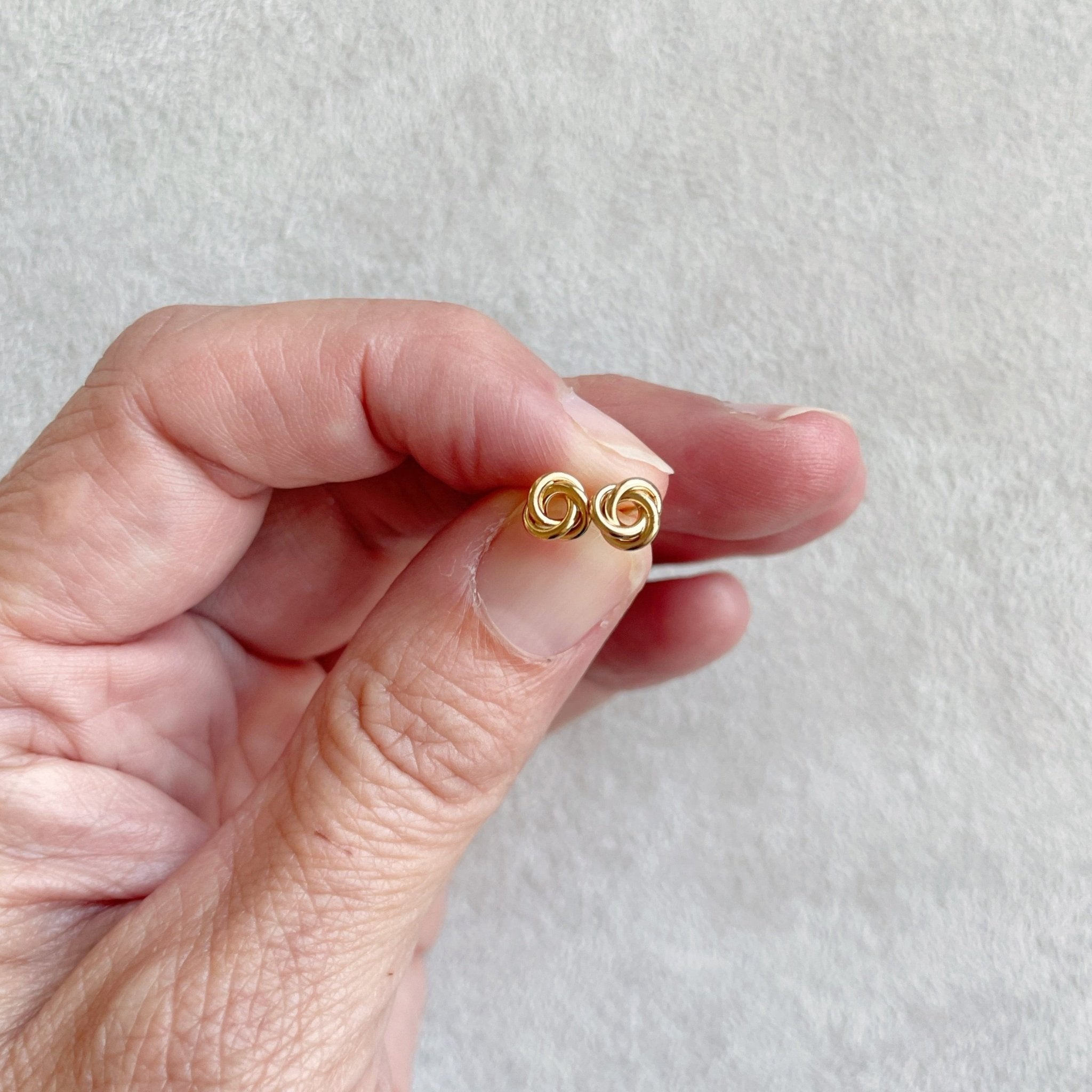 Hand holding 6 mm gold love knot stud earrings. Love Knot Studs by Sarah Cornwell Jewelry