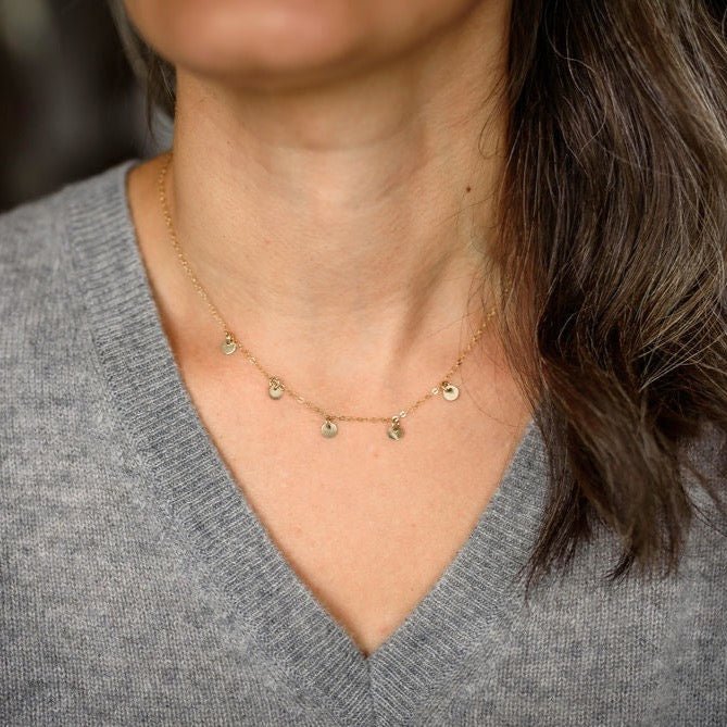 Woman's neckline wearing gray v neck sweater with gold necklace with 5 tiny gold discs. Mae Necklace by Sarah Cornwell Jewelry