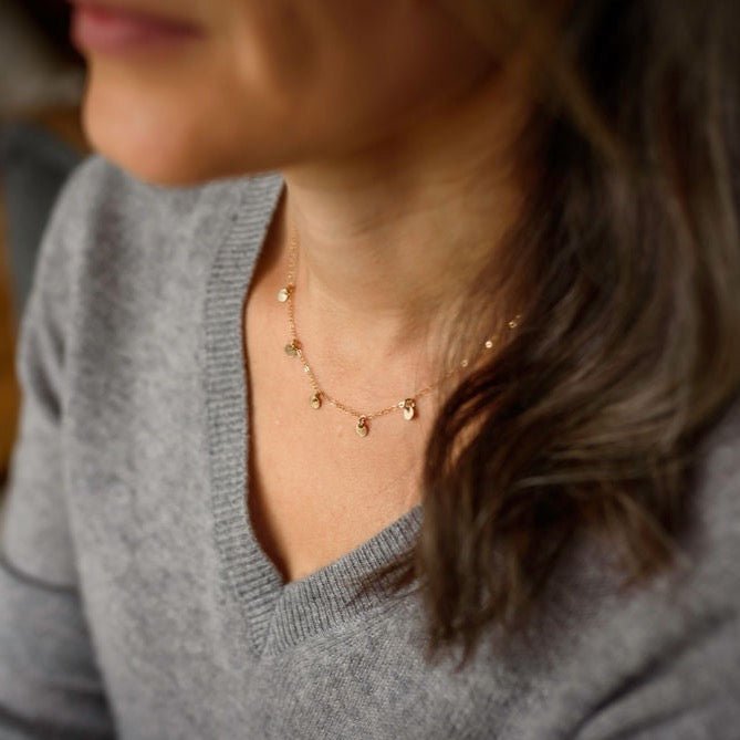 Woman's neckline wearing gray v neck sweater with gold necklace with 5 tiny gold discs. Mae Necklace by Sarah Cornwell Jewelry