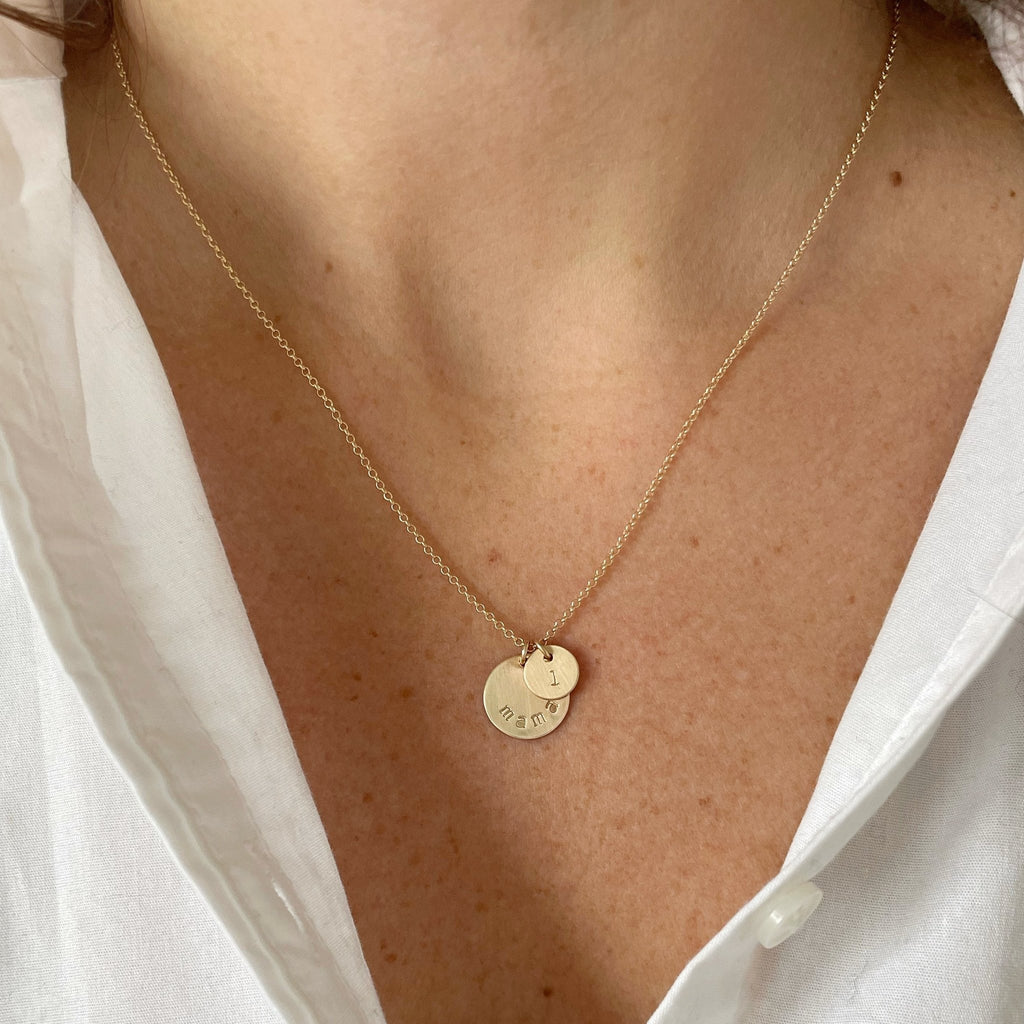 Woman's neck wearing white button down with gold mama stamped disc necklace with a tiny stamped initial disc. Mama Necklace by Sarah Cornwell Jewelry