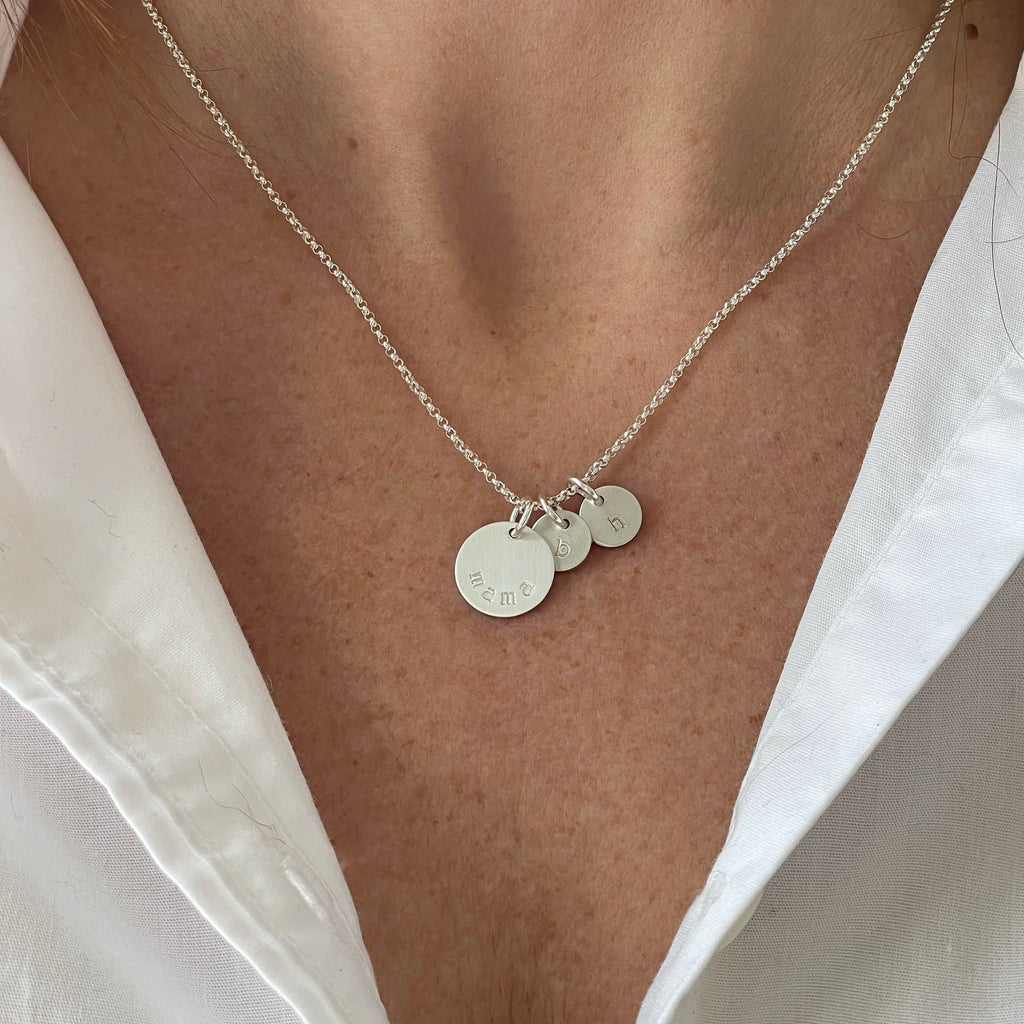 Woman's neck wearing white button down with silver mama stamped disc necklace with 2 tiny stamped initial discs. Mama Necklace by Sarah Cornwell Jewelry