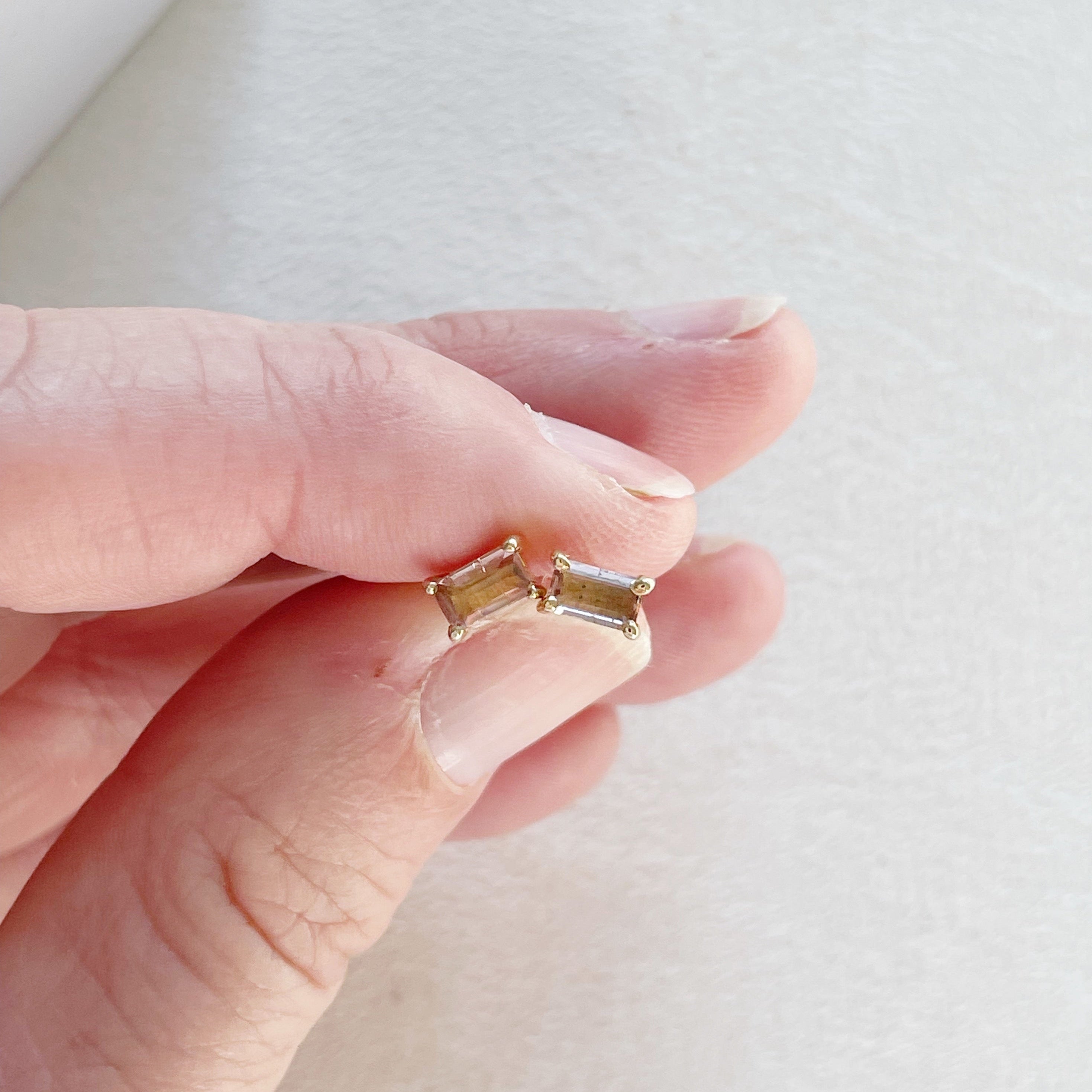 Woman's hand holding 14K gold and 1 carat rectangular cut peach pink tourmaline stud earrings. Michelle Studs by Sarah Cornwell Jewelry