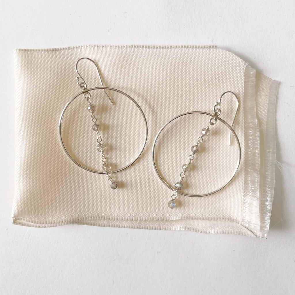 Silver Nantucket Earrings by Sarah Cornwell Jewelry. Sparkly statement silver hoop earrings with a strand of 5 wire wrapped labradorite gemstones down the middle on a white background.