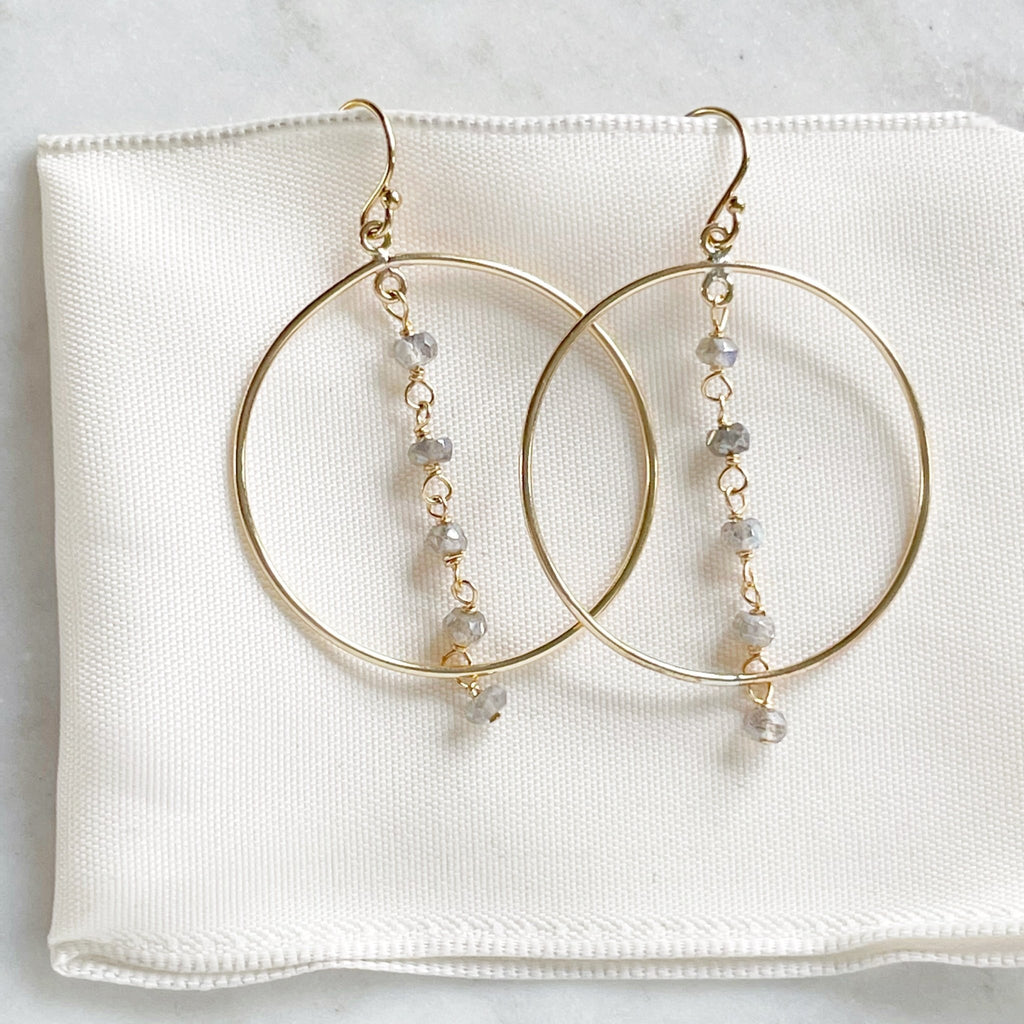 Gold Nantucket Earrings by Sarah Cornwell Jewelry. Sparkly statement gold hoop earrings with a strand of 5 wire wrapped labradorite gemstones down the middle on a white background.