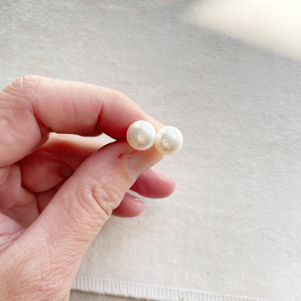 Hand holding oversized 9.5-10 mm creamy white oyster pearl stud earrings. Oyster Pearl Studs by Sarah Cornwell Jewelry