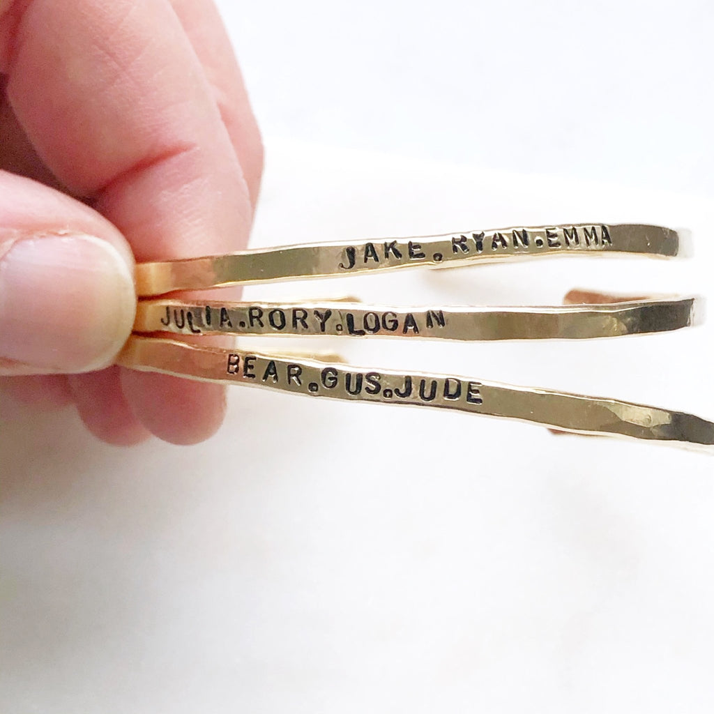 Fingers holding 3 gold textured bangle bracelets with stamped personalization on the outside. Personalized Caroline Bangle by Sarah Cornwell Jewelry