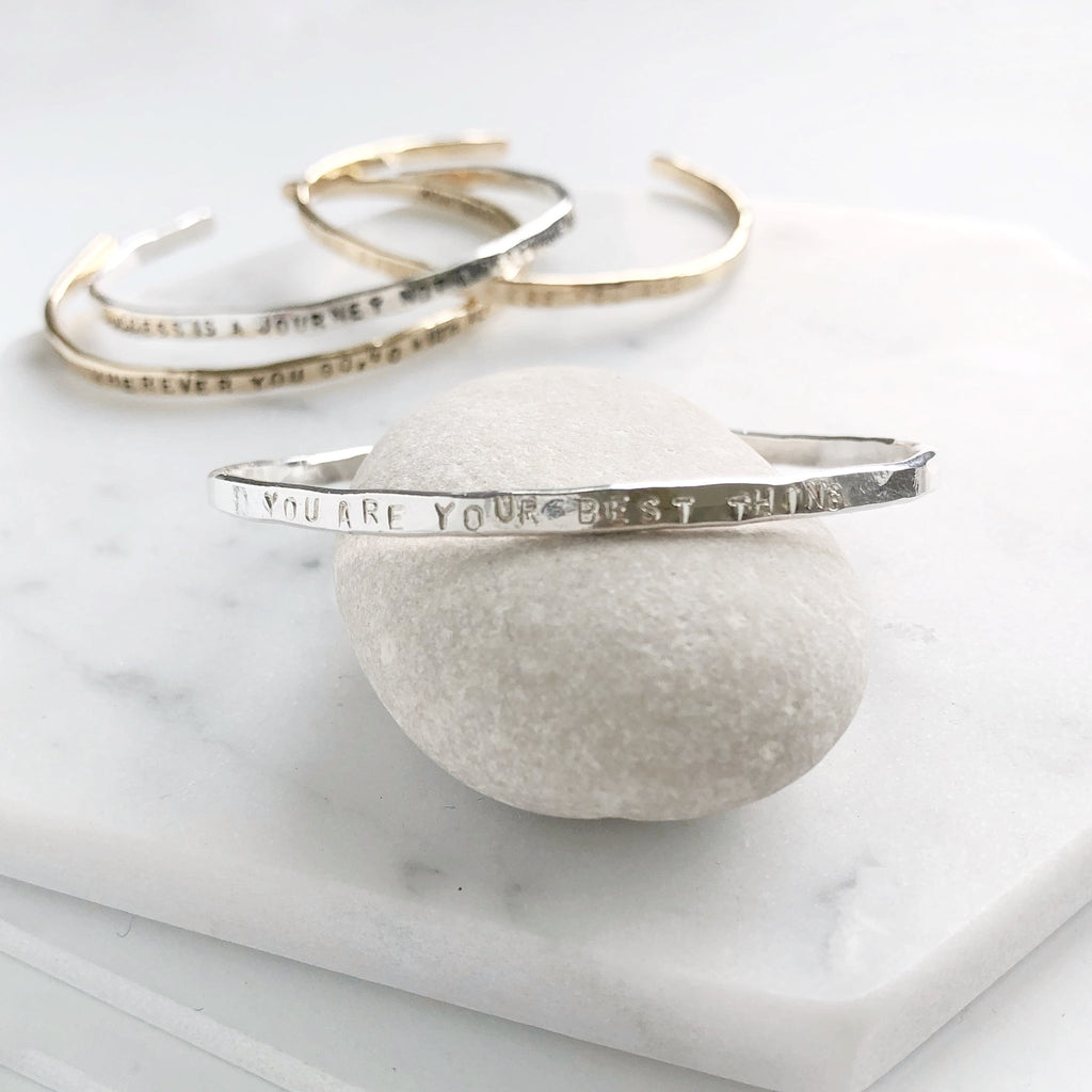 4 gold textured bangle bracelets with stamped personalization on the outside on a light gray rock. Personalized Caroline Bangle by Sarah Cornwell Jewelry