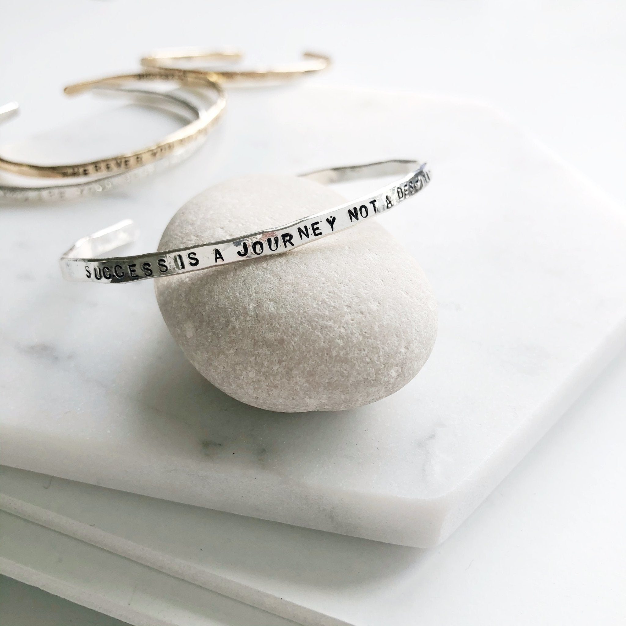 4 gold textured bangle bracelets with stamped personalization on the outside on a light gray rock. Personalized Caroline Bangle by Sarah Cornwell Jewelry