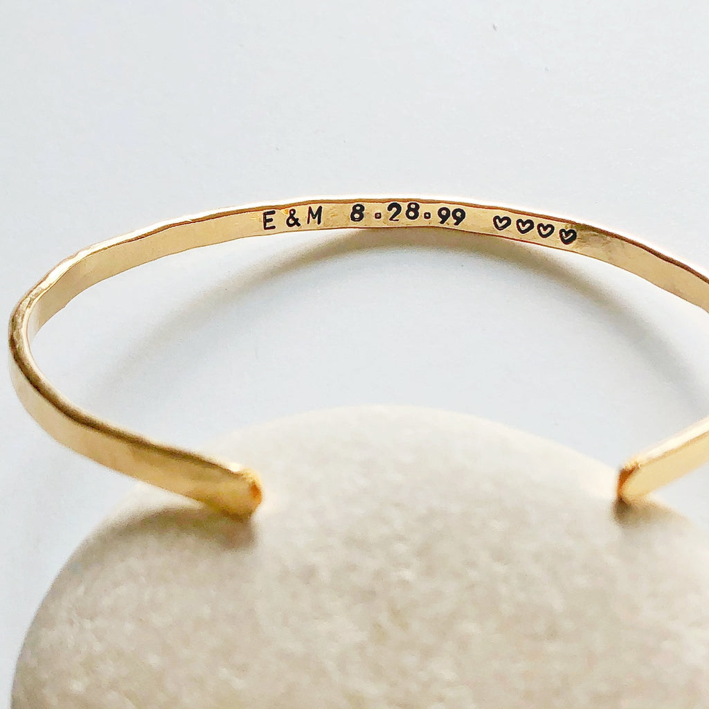 Gold textured bangle bracelet with stamped personalization on the inside on a light gray rock. Personalized Caroline Bangle by Sarah Cornwell Jewelry