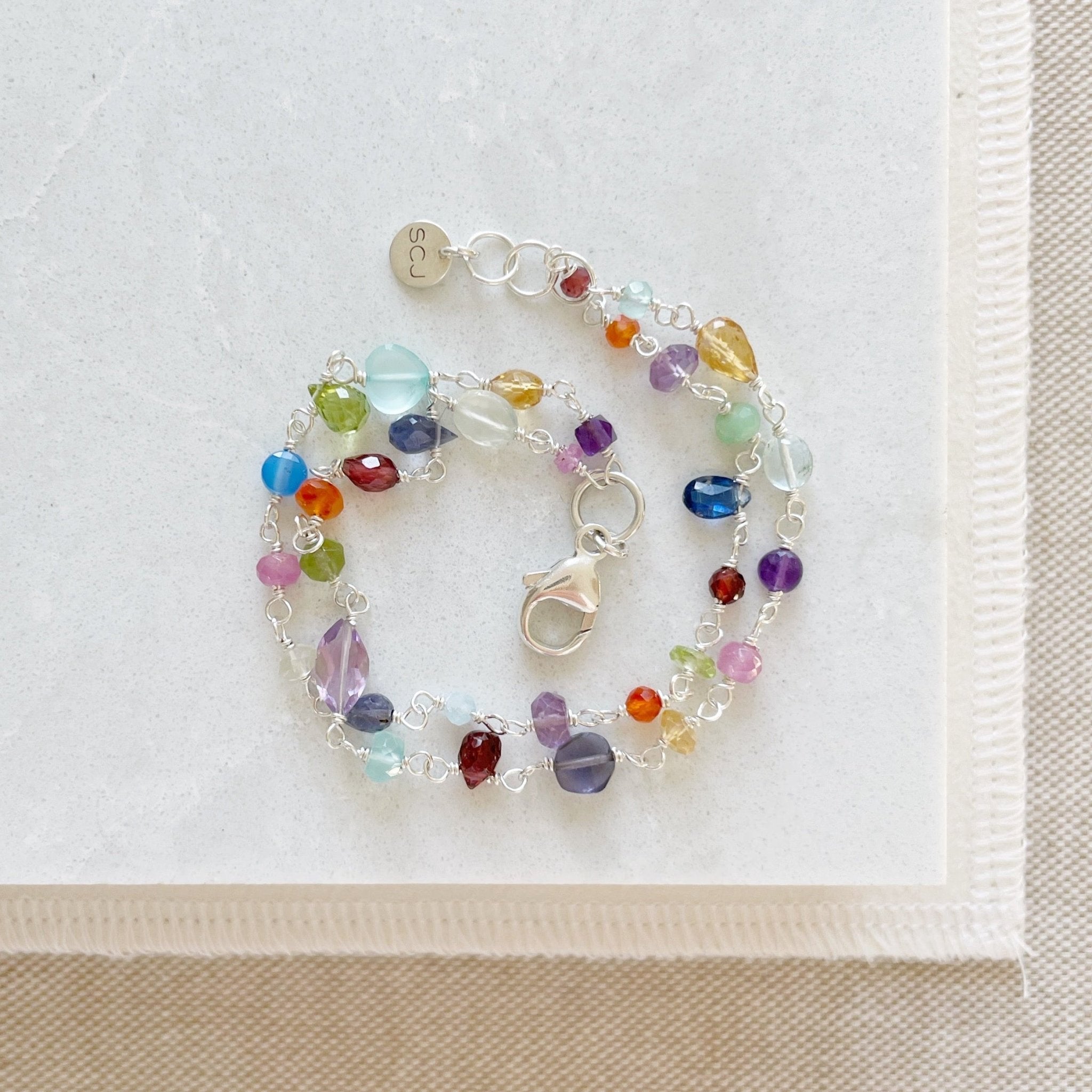 Silver and rainbow gemstone bracelet with wire wrapped aquamarine, peridot, quartz, amethyst, sapphires, chalcedony, citrine, smokey quartz, garnet, and labradorite gemstones. Poppy Love Bracelet by Sarah Cornwell Jewelry