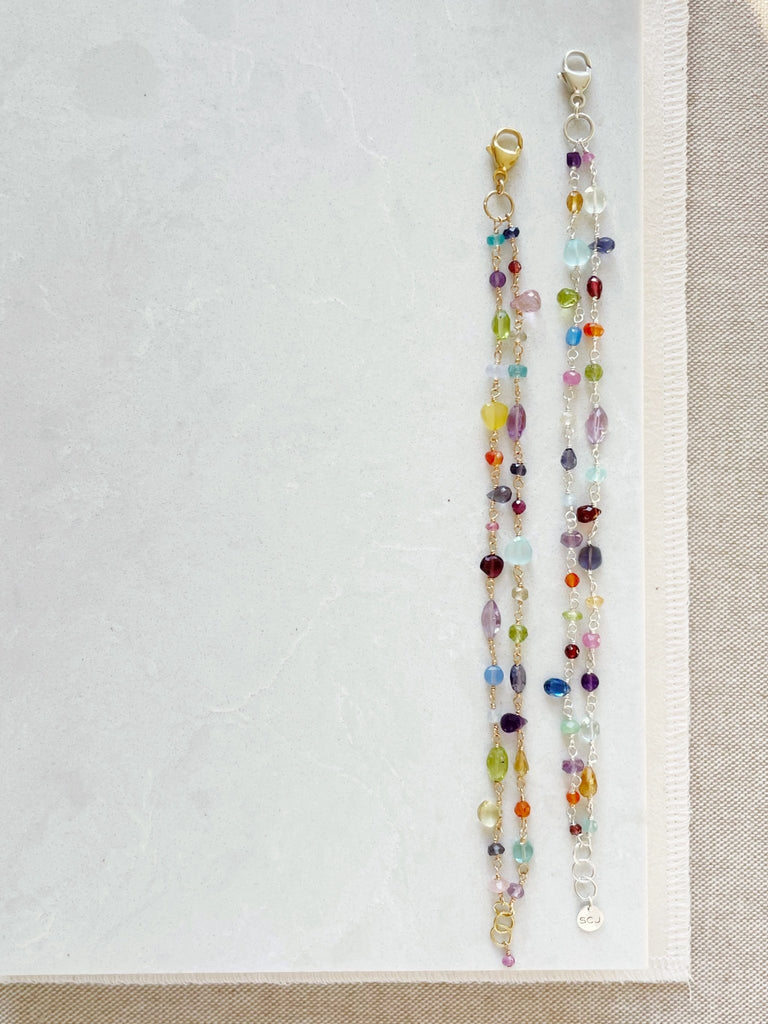 2 Gold and silver rainbow gemstone bracelets with wire wrapped aquamarine, peridot, quartz, amethyst, sapphires, chalcedony, citrine, smokey quartz, garnet, and labradorite gemstones. Poppy Love Bracelet by Sarah Cornwell Jewelry