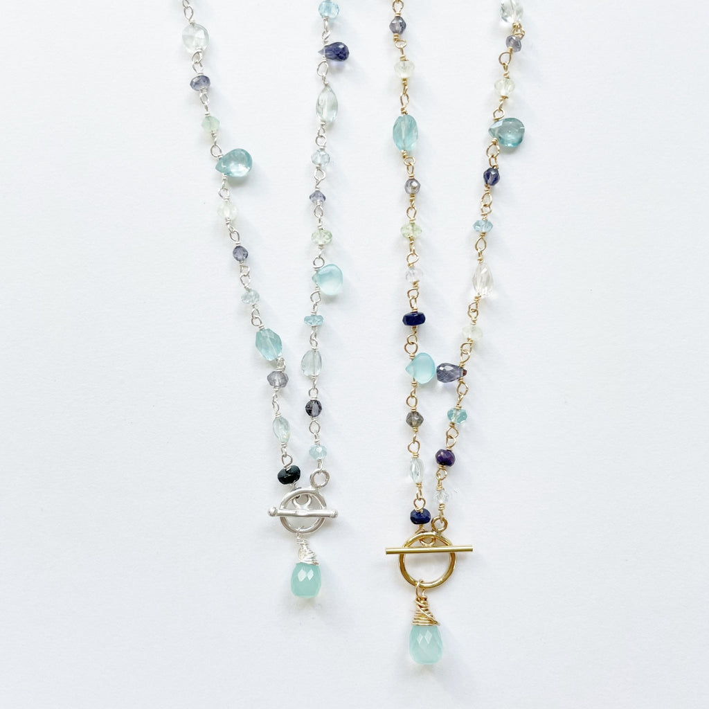 Gold and silver 18 inch gemstone necklaces with wire wrapped blue chalcedony, aqua chalcedony, prehnite, iolite, blue sapphires, and aquamarine gemstones with a front toggle closure and large chalcedony drop. Poppy Seaside Front Toggle by Sarah Cornwell Jewelry