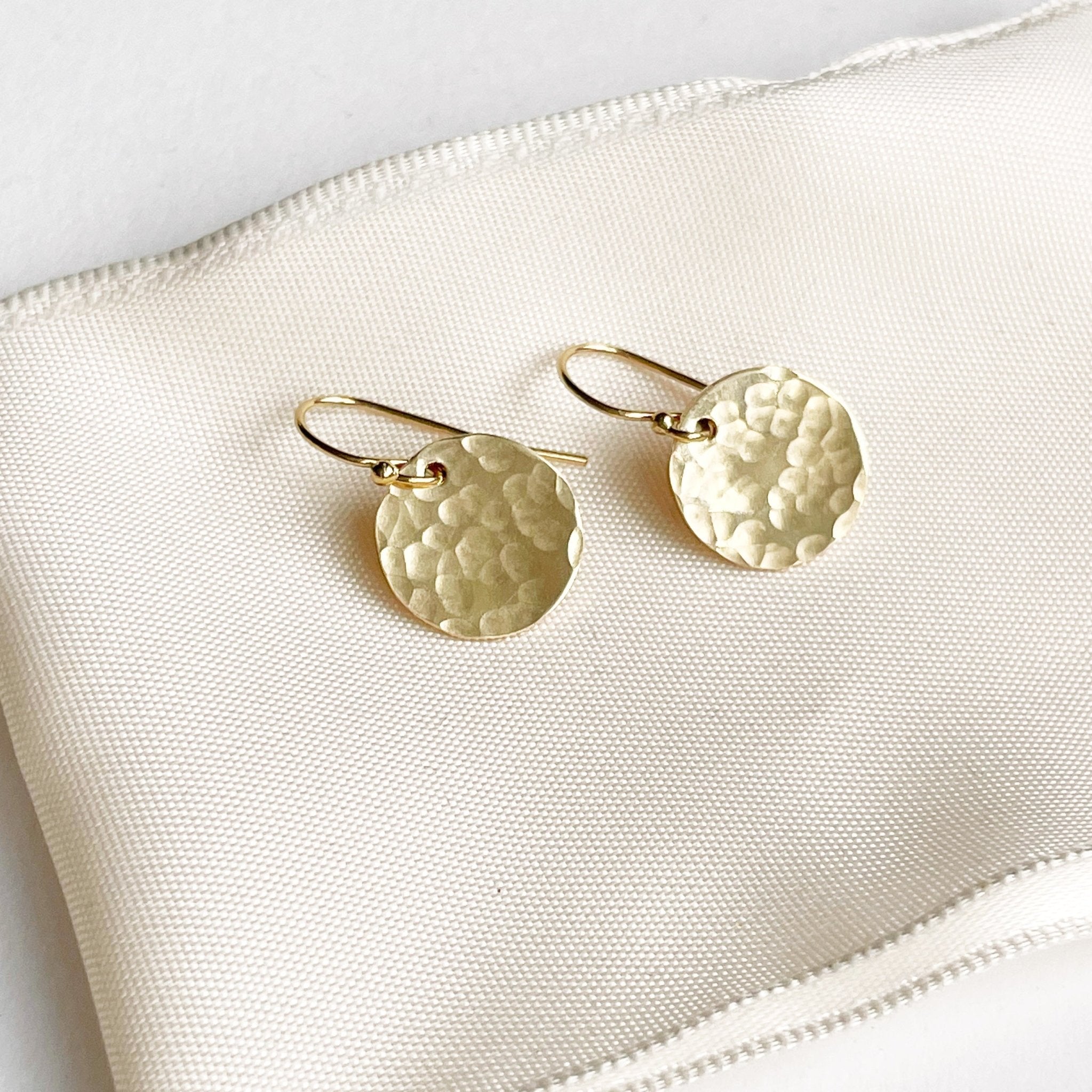 Gold Rachel Earrings by Sarah Cornwell Jewelry. Shimmery, dainty gold 1/2 inch textured disc earrings on a cream background.