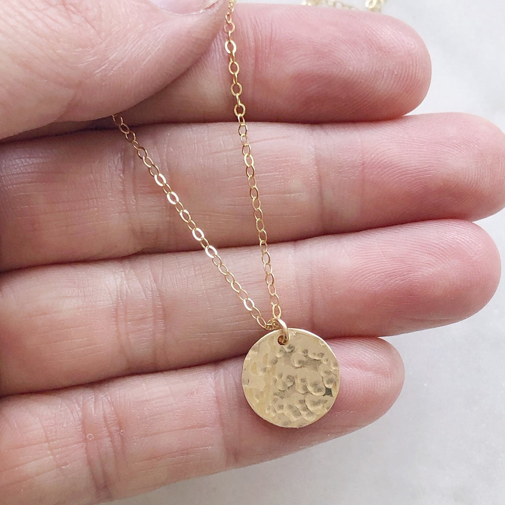 Hand holding gold textured disc necklace. Ross Necklace by Sarah Cornwell Jewelry