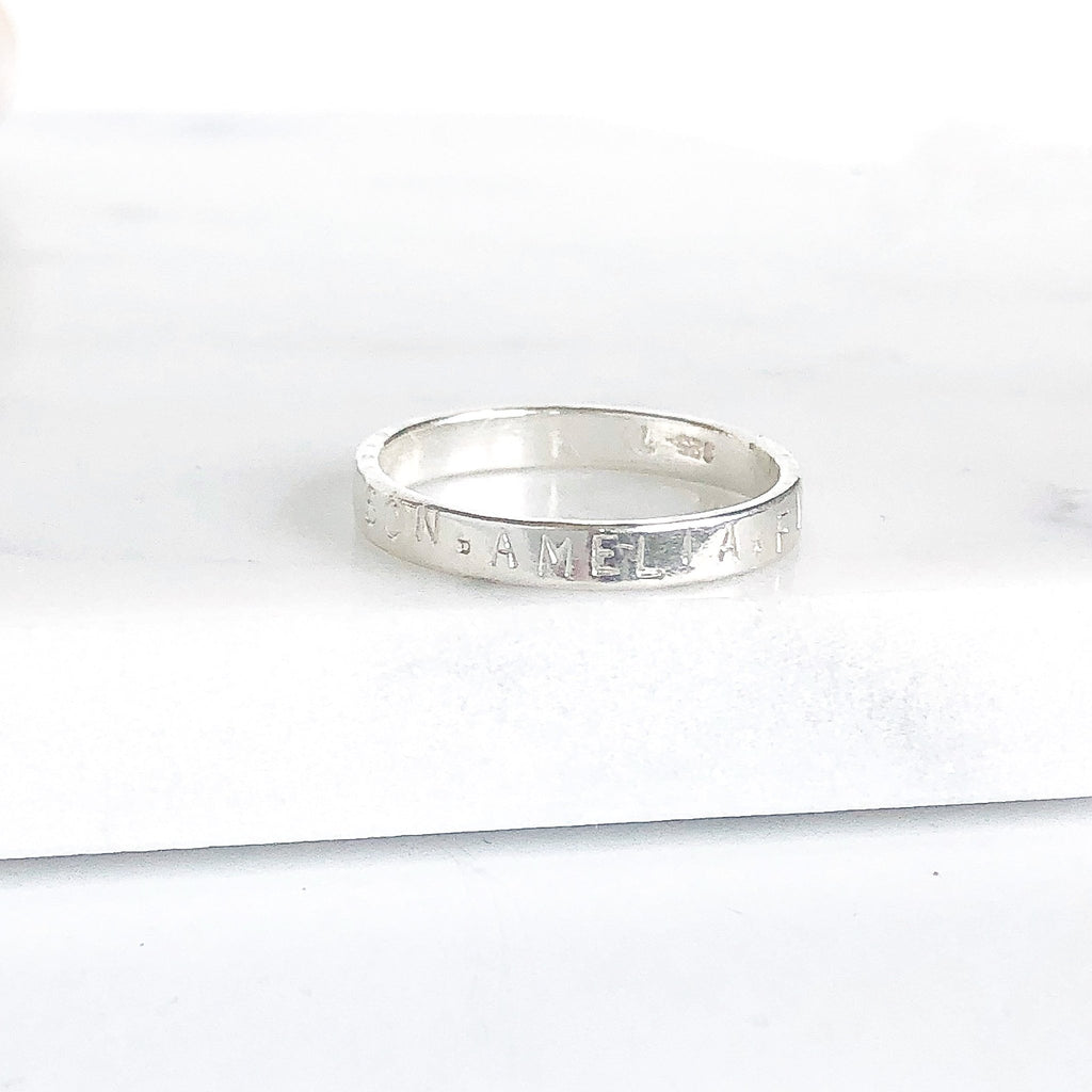 Silver ring stamped with names in capital letters. Ruby Ring by Sarah Cornwell Jewelry
