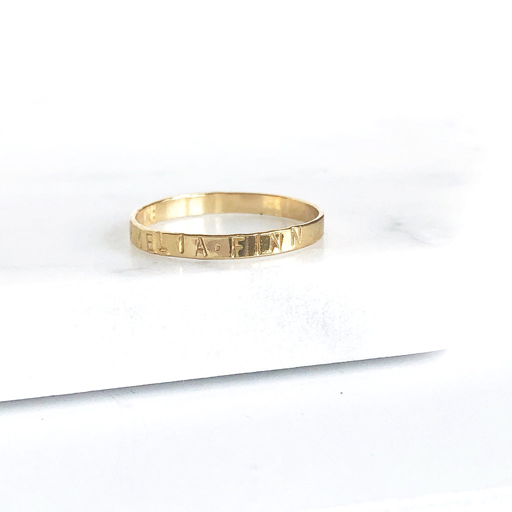 Gold ring stamped with names in capital letters. Ruby Ring by Sarah Cornwell Jewelry