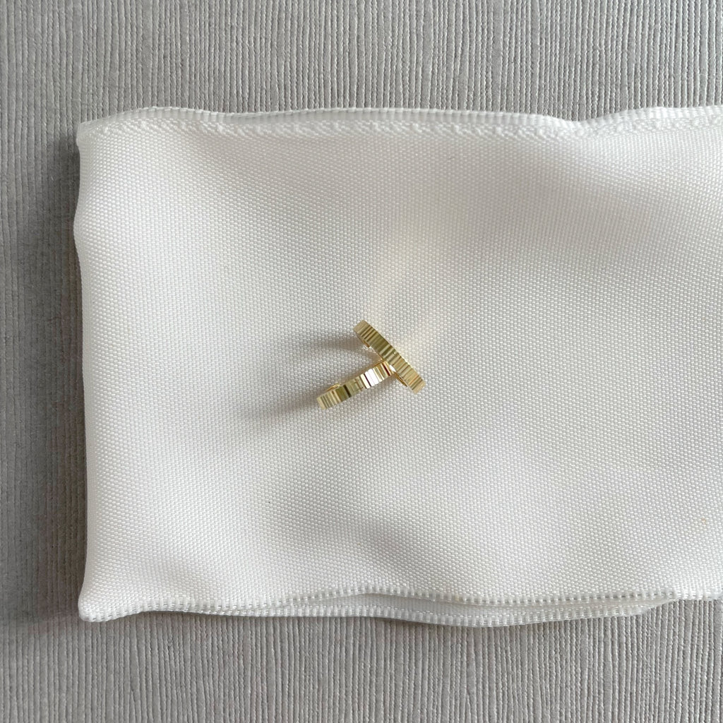 Solid Gold Ruth Huggies by Sarah Cornwell Jewelry. Solid gold tiny hoop huggie earrings on a white and gray background.