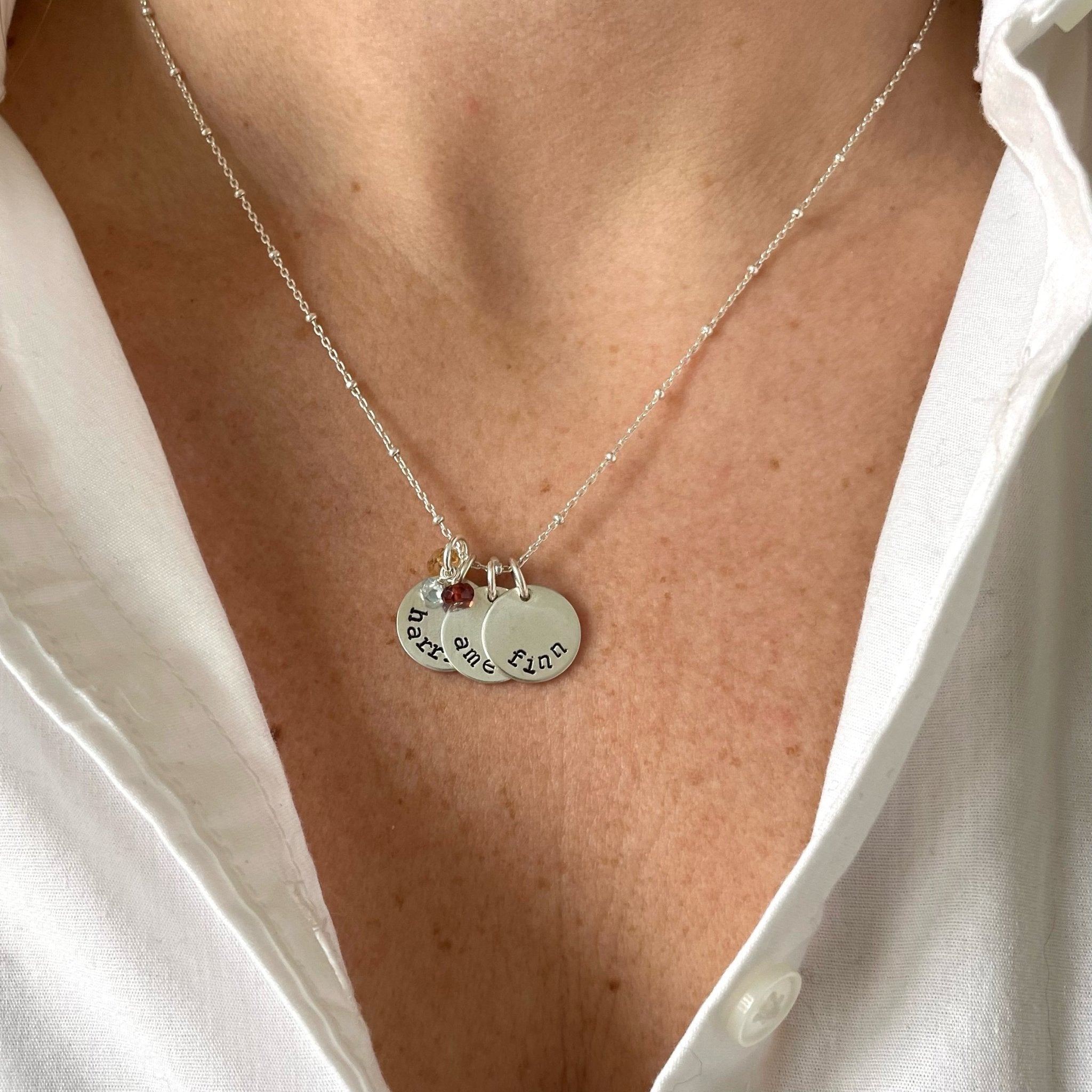 Woman's neckline with white button down and silver stamped disc necklace with link ball chain and 3 personalized stamped name discs and wire wrapped birthstones. Stella Necklace by Sarah Cornwell Jewelry