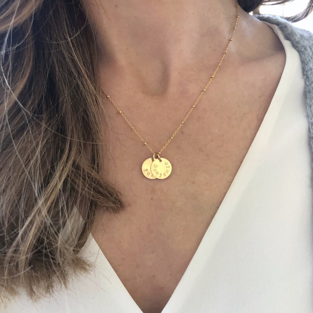 Woman's neckline with white shirt and gold stamped disc necklace with link ball chain and 2 personalized stamped name discs. Stella Necklace by Sarah Cornwell Jewelry