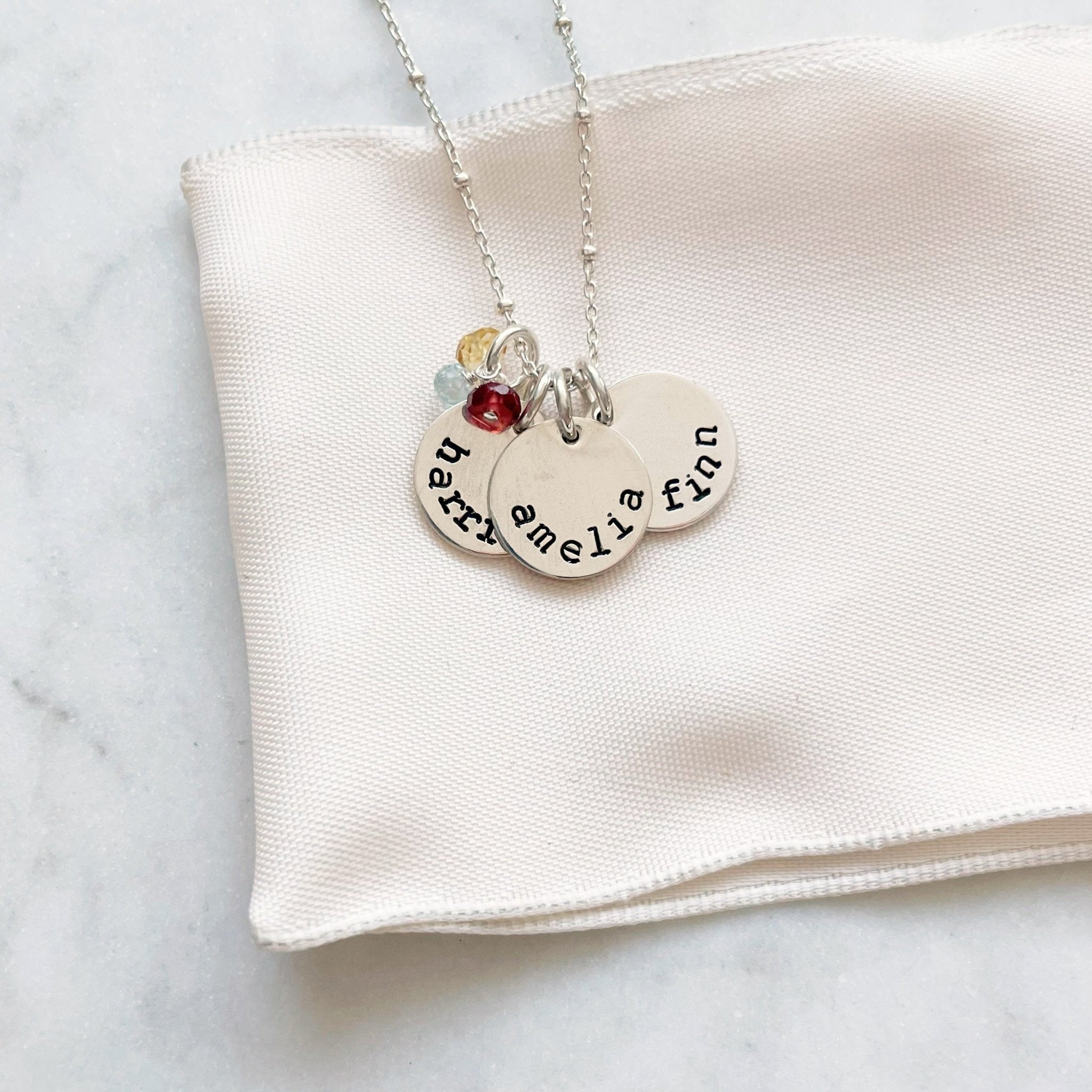 Silver stamped disc necklace with link ball chain and 3 personalized stamped name discs and 3 wire wrapped birthstone gemstones. Stella Necklace by Sarah Cornwell Jewelry