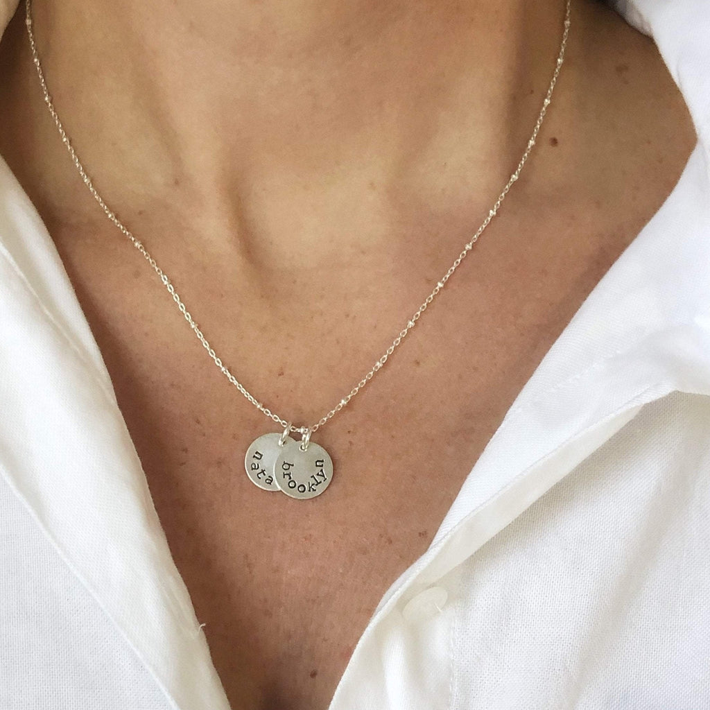 Woman's neckline with white button down and silver stamped disc necklace with link ball chain and 2 personalized stamped name discs. Stella Necklace by Sarah Cornwell Jewelry