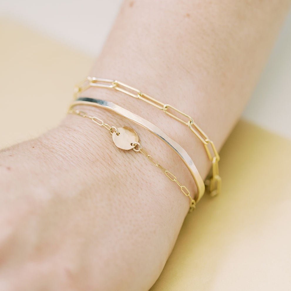 Close up of woman's wrist wearing gold large link chain bracelet, gold textured disc bracelet and gold bangle. Sunny Bracelet by Sarah Cornwell Jewelry