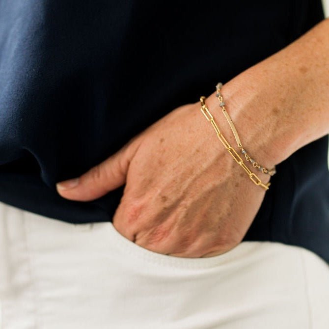Close up of woman's wrist wearing white pants and navy top with gold large link chain bracelet and gold bar and gemstone bracelet. Sunny Bracelet by Sarah Cornwell Jewelry
