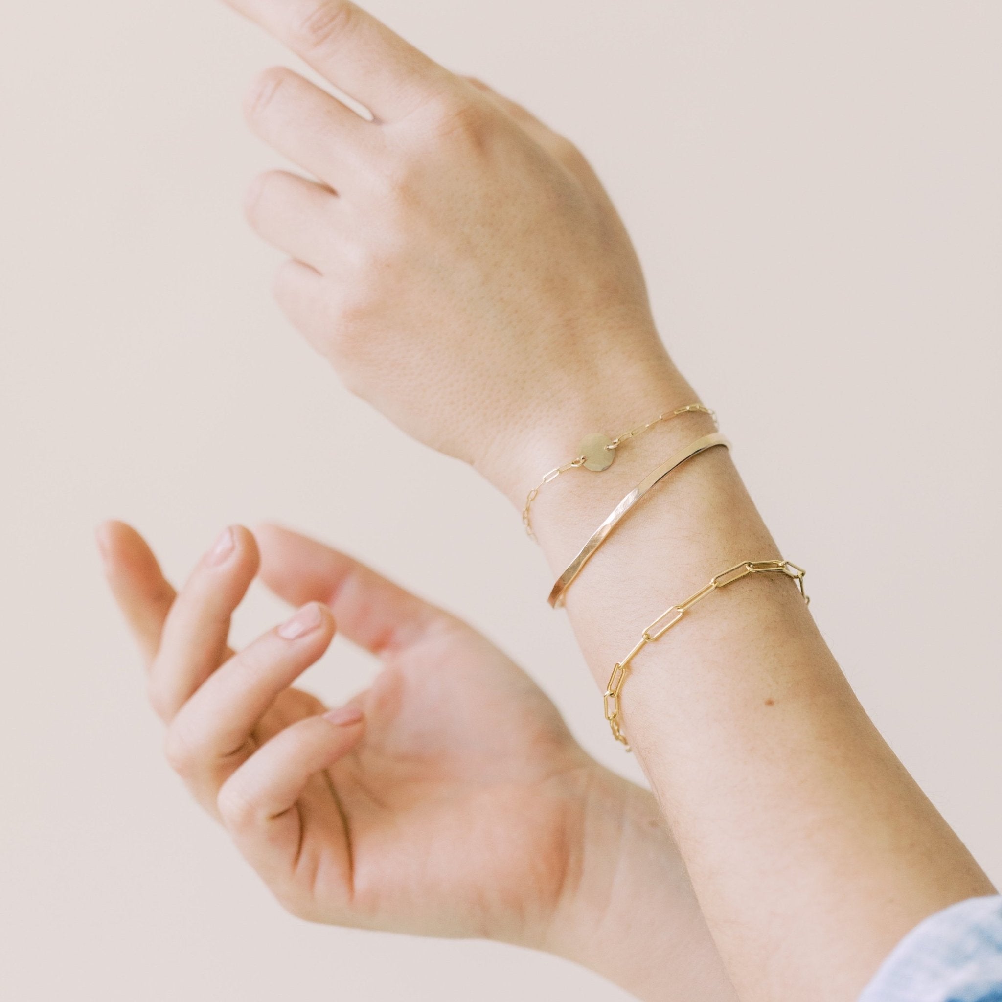 Close up of woman's wrists wearing gold large link chain bracelet, gold textured disc bracelet and gold bangle. Sunny Bracelet by Sarah Cornwell Jewelry