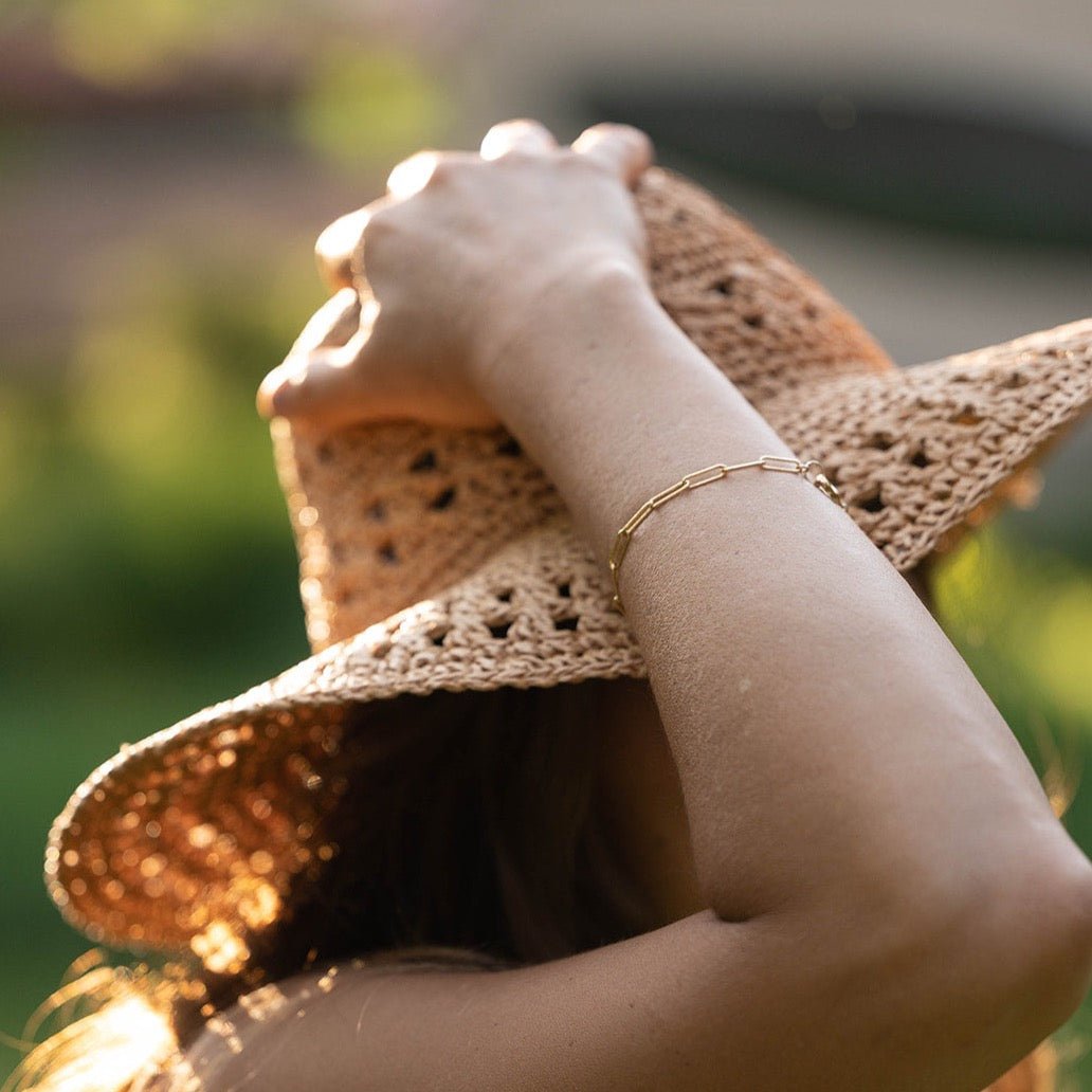 Close up of woman's wrist wearing straw hat and gold large link chain bracelet. Sunny Bracelet by Sarah Cornwell Jewelry