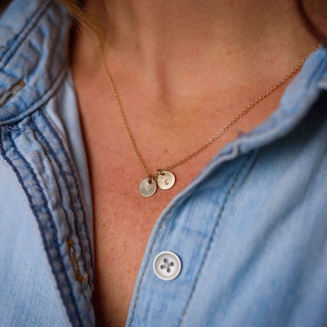 Woman's neckline wearing denim button down with gold stamped disc personalized initial necklace with 2 gold stamped discs with initials. Tabby Necklace by Sarah Cornwell Jewelry