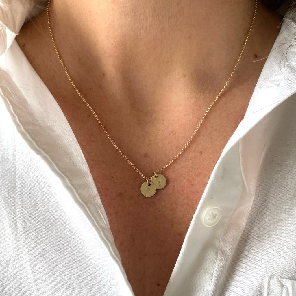Woman's neckline wearing white button down with gold stamped disc personalized initial necklace with 2 gold stamped discs with initials. Tabby Necklace by Sarah Cornwell Jewelry