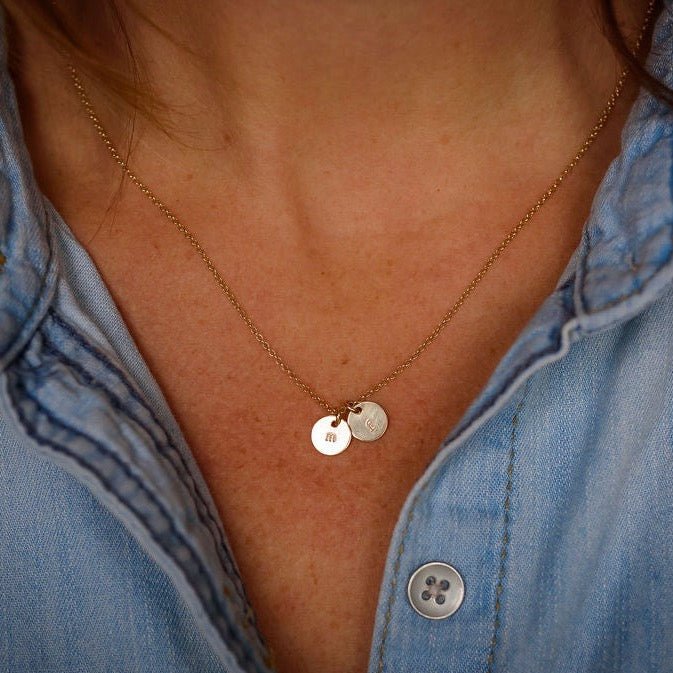 Woman's neckline wearing denim button down with gold stamped disc personalized initial necklace with 2 gold stamped discs with initials. Tabby Necklace by Sarah Cornwell Jewelry