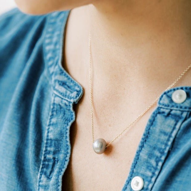 Close up of woman's neckline wearing denim top with gold chain necklace with single large silver gray freshwater pearl. Tomlin Necklace by Sarah Cornwell Jewelry