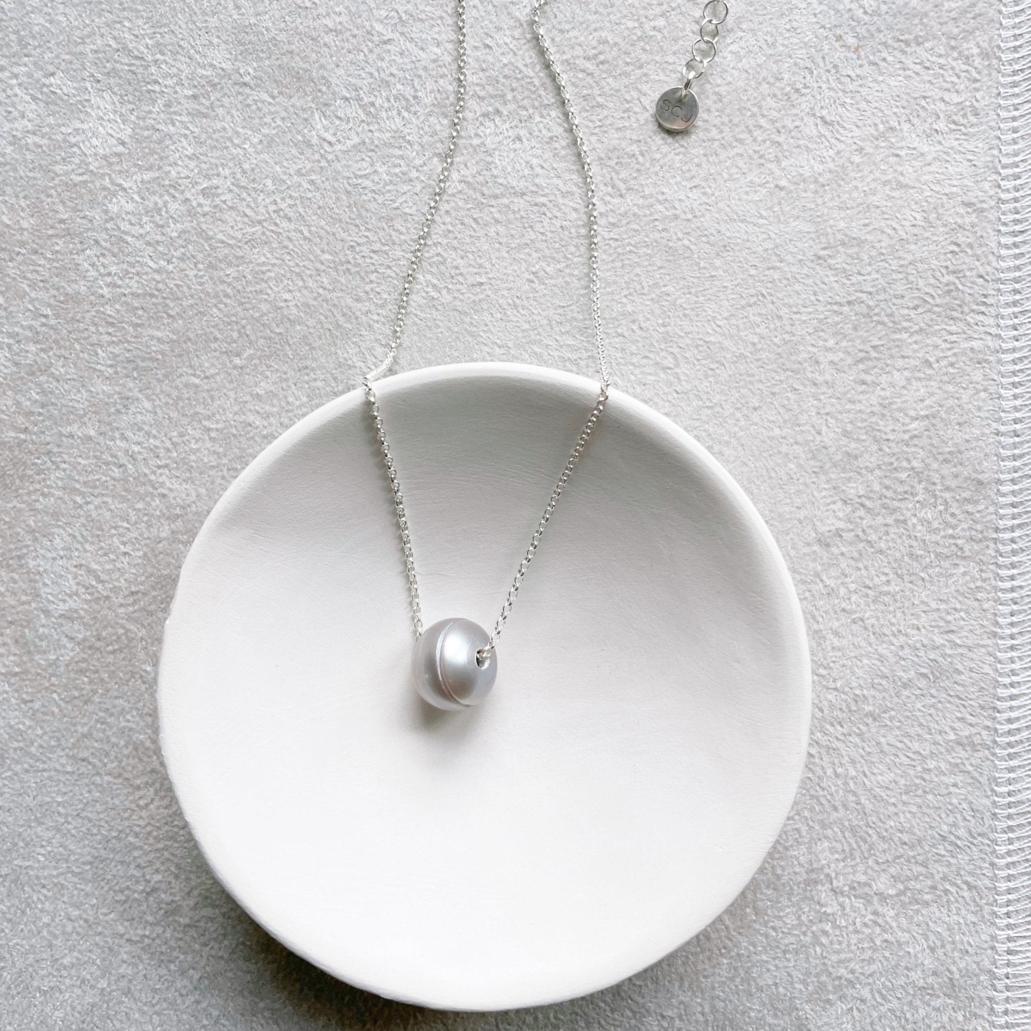 Silver chain necklace with single large silver gray freshwater pearl in white dish. Tomlin Necklace by Sarah Cornwell Jewelry